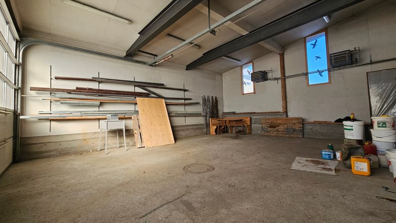 empty garage, large shelves, wooden planks, small table, concrete floor, multiple windows