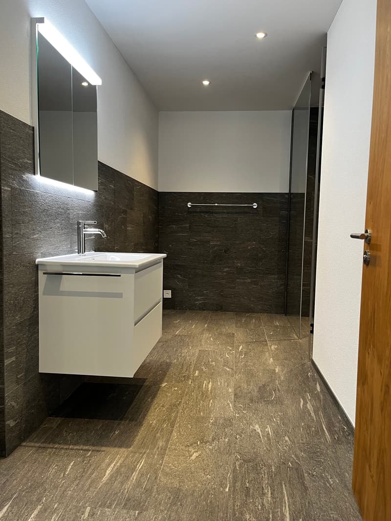 modern minimalist bathroom with white sink, silver faucet, mirror, black walls, gray tiled floor, glass shower enclosure