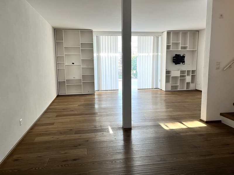 Empty room with wooden floor, white walls, two white shelves, sliding glass doors, and a central pillar.