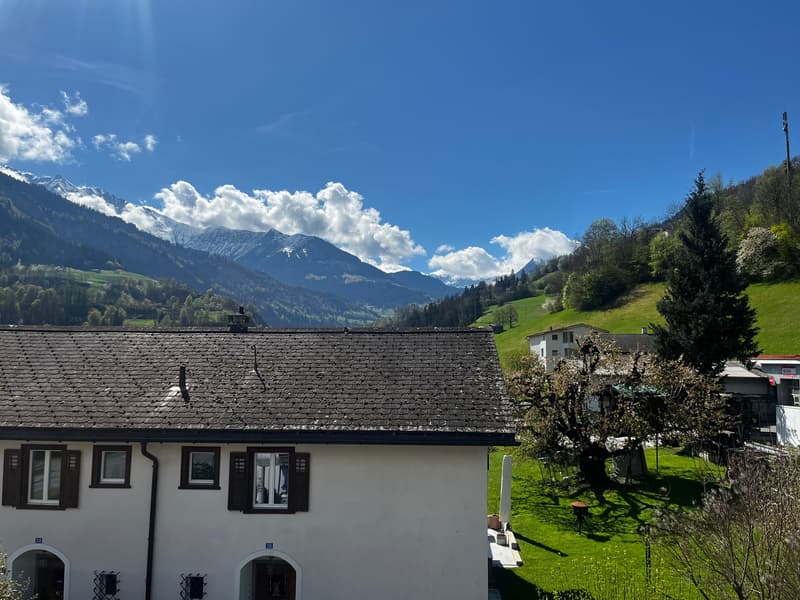 white house, brown roof, windows with shutters, green lawn, mountains in the background