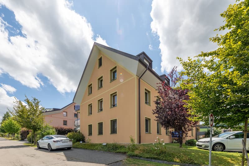2 story building, beige exterior, multiple windows, parking area, trees, shrubs