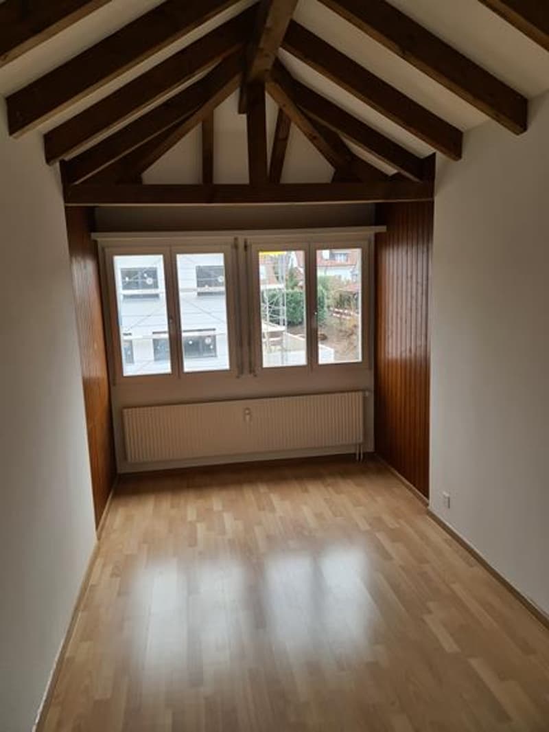 Spacious room with high vaulted ceiling, wooden beams, and large windows providing natural light. Hardwood flooring throughout.