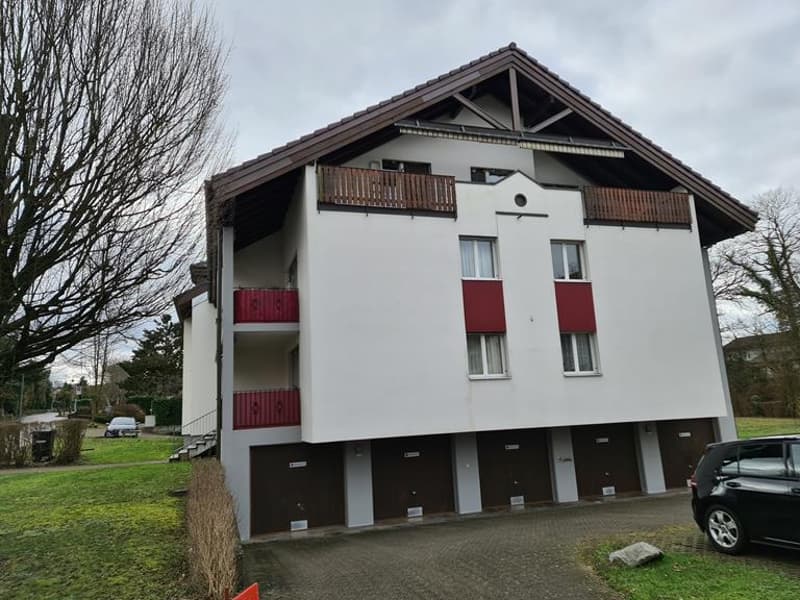 3-story apartment building with white exterior, red balcony railings, and covered parking spaces on the ground floor