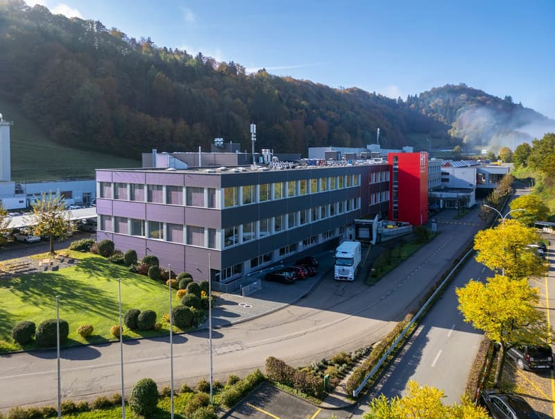 office building with glass windows, parking area, greenery, surrounding hills