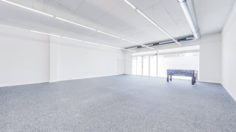 empty room with gray carpet, white walls, ceiling lamps, foosball table, glass door
