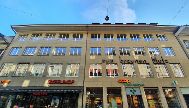 A multi-story commercial building with a distinctive facade featuring large windows and signage for various businesses, including Ryffliof and Coop vitality-apotheke.