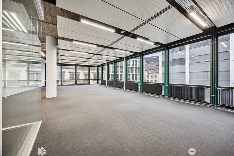 Empty office with large glass windows, carpeted floor, modern ceiling and large pillars.