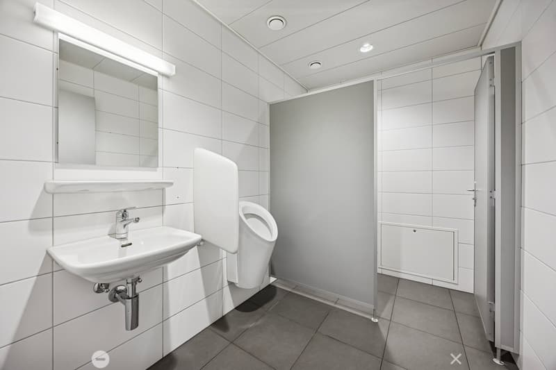white tiled wall and floor, stainless steel urinal, white vanity sink with faucet, a mirror on the wall, a door