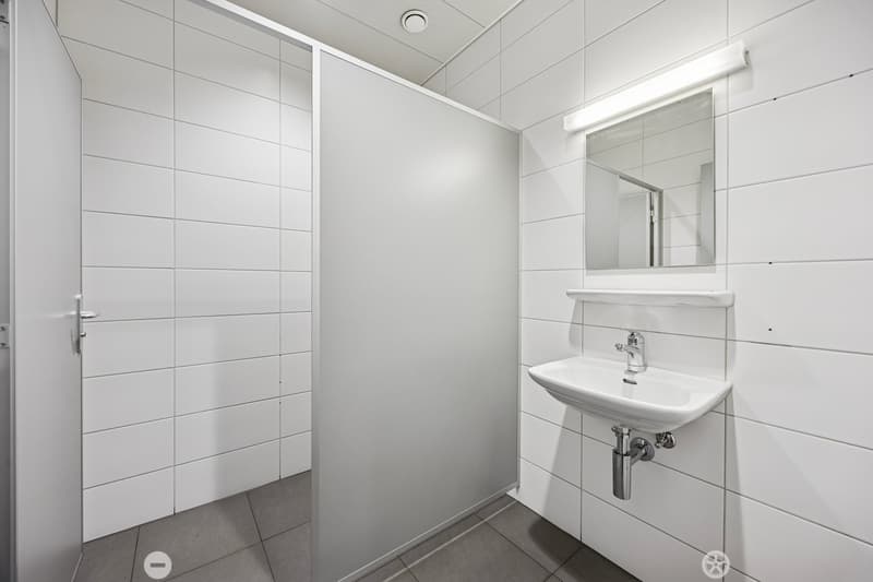 A small bathroom with white tiles, a sink, a mirror, and a shower area.