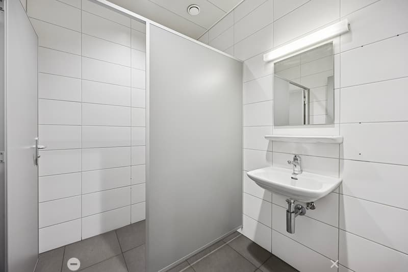 A small bathroom with white tiles, a sink, a mirror, and a shower area.
