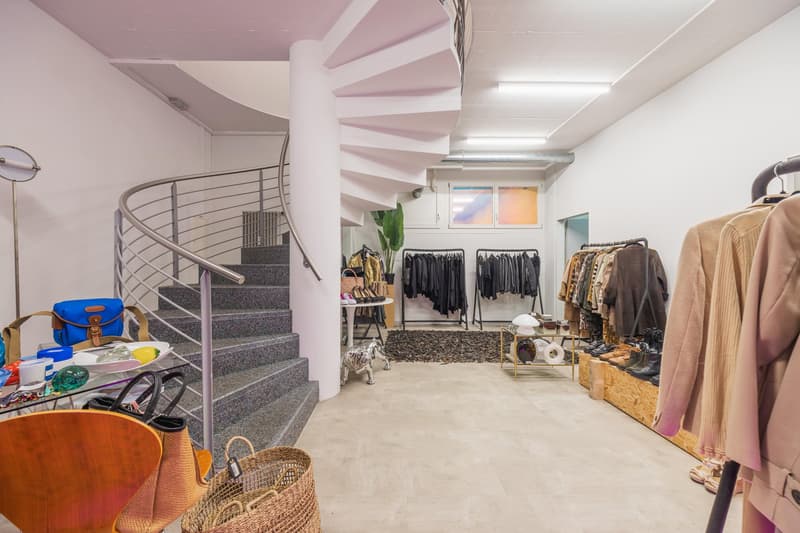 large open space, spiral staircase, racks with clothing, glass table with items