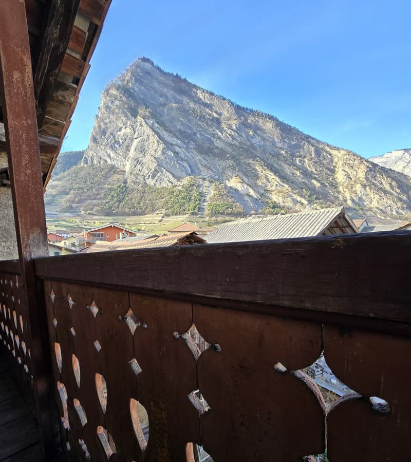 Rustic balcony with wooden railings and mountain view.