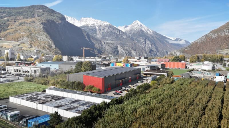 A large commercial building complex with several buildings, mountains in the background, large open areas, and cars parked in front.