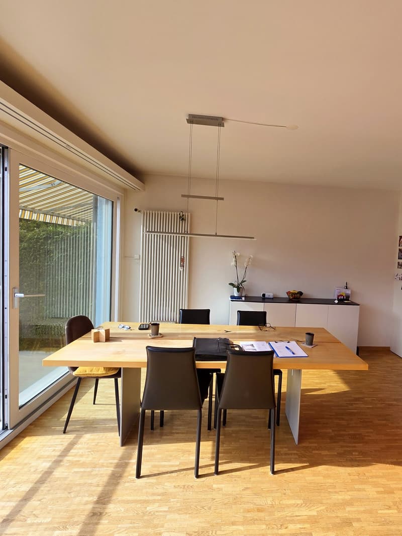 a dining table with 4 chairs, a long table, a cabinet with various items, sliding glass door, wooden flooring, ceiling lamp