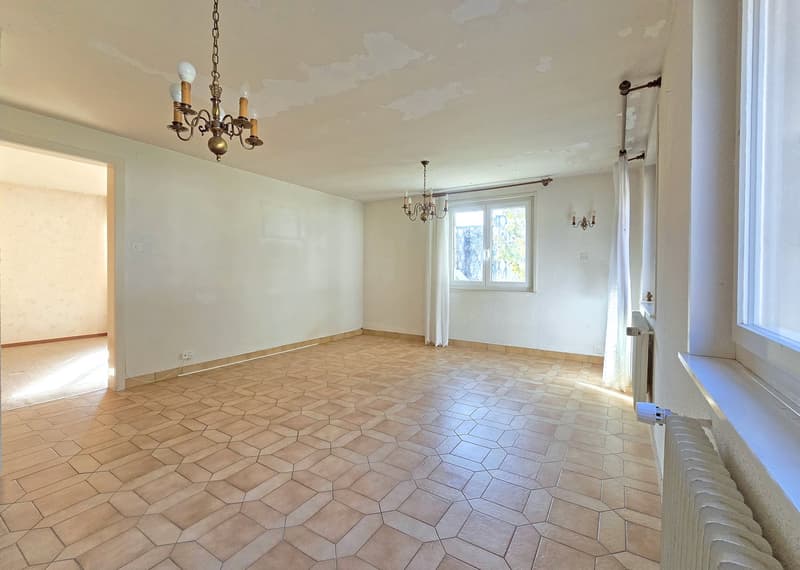 Empty room with white walls, tiled floor, two chandeliers, window with white curtains, radiator