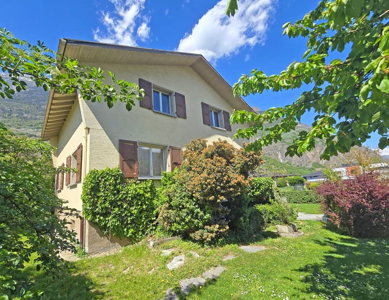 2 story house, beige exterior, brown shutters, surrounded by greenery, mountain view