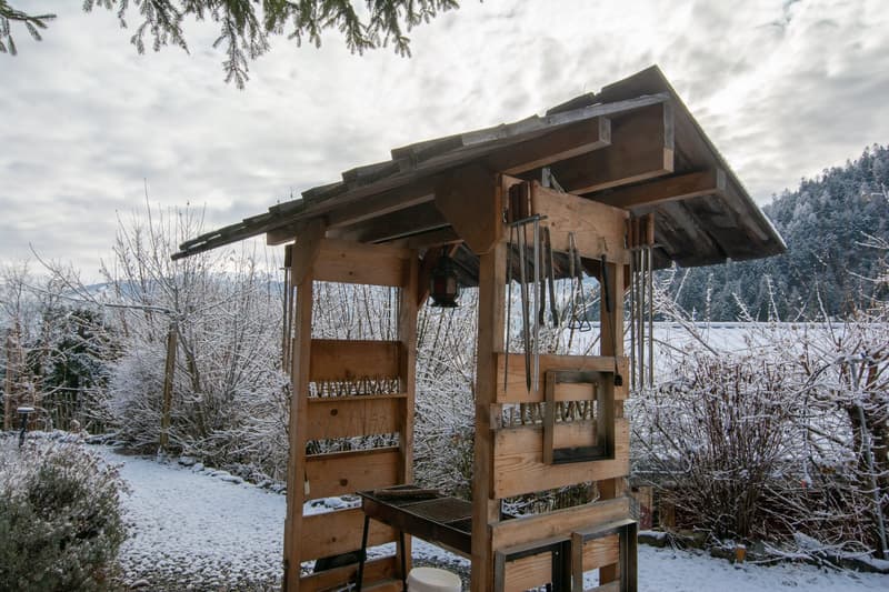 Wooden structure in garden, tools hanging on wall, snow covering ground