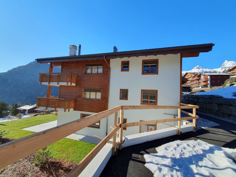 modern apartment building, wooden balconies, white walls, brown roof, surrounded by mountains and snow
