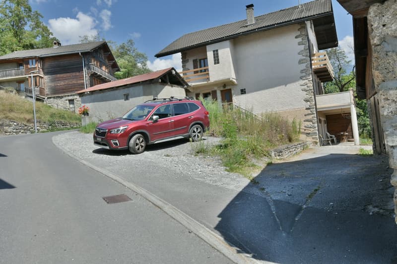 two-story wooden houses, red SUV parked in front, gravel driveway, street with a slope, balcony on one house