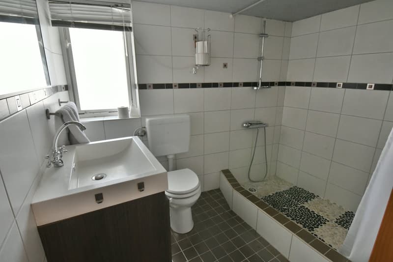 white tiled walls, white toilet, sink, walk-in shower