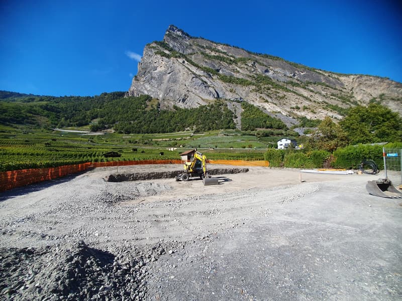 Empty construction site, gravel, machinery in the center, vineyard at the back, mountain at the far back
