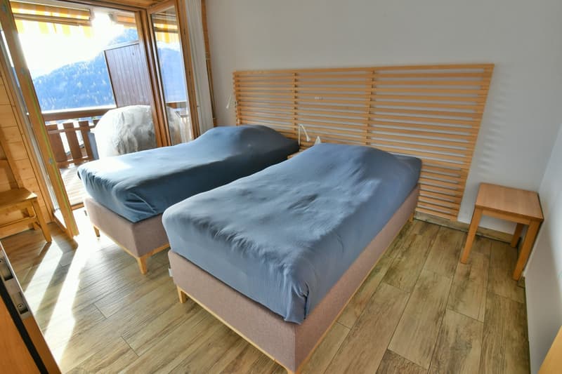 wooden floor, two double beds, blue covers, wooden headboards, side tables, glass doors, balcony with railing, mountain view