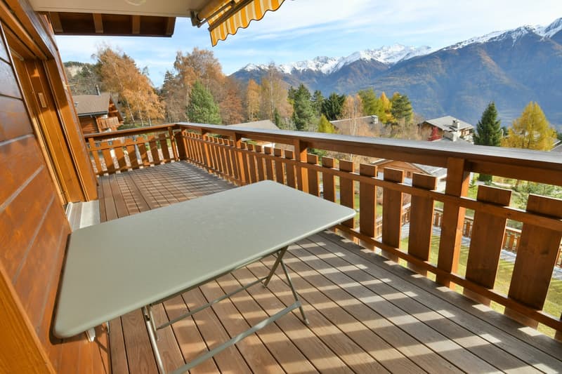 Balcony with wooden flooring, wooden railing, a table and mountain view