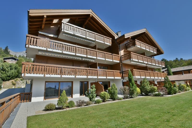 Wooden building, 3 stories, balconies, large windows, front yard with plants and lawn