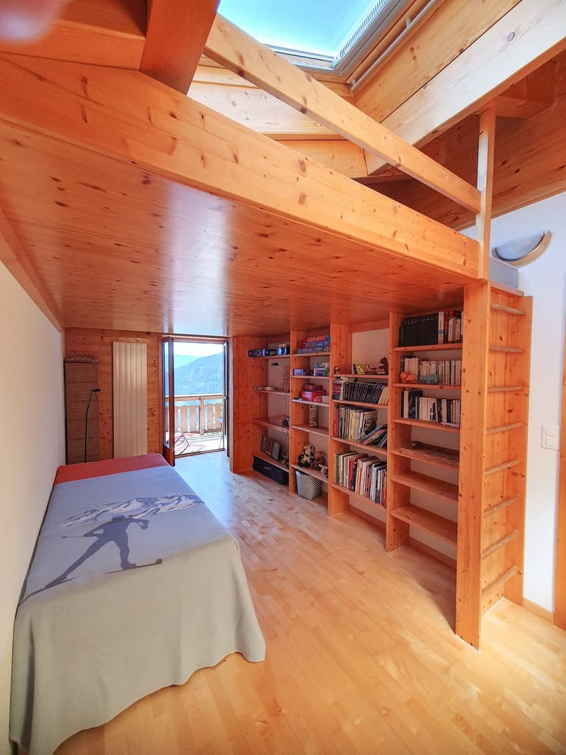 wooden walls and ceiling, bed with grey blanket, bookshelf, items on the shelf, window with terrace, floor view