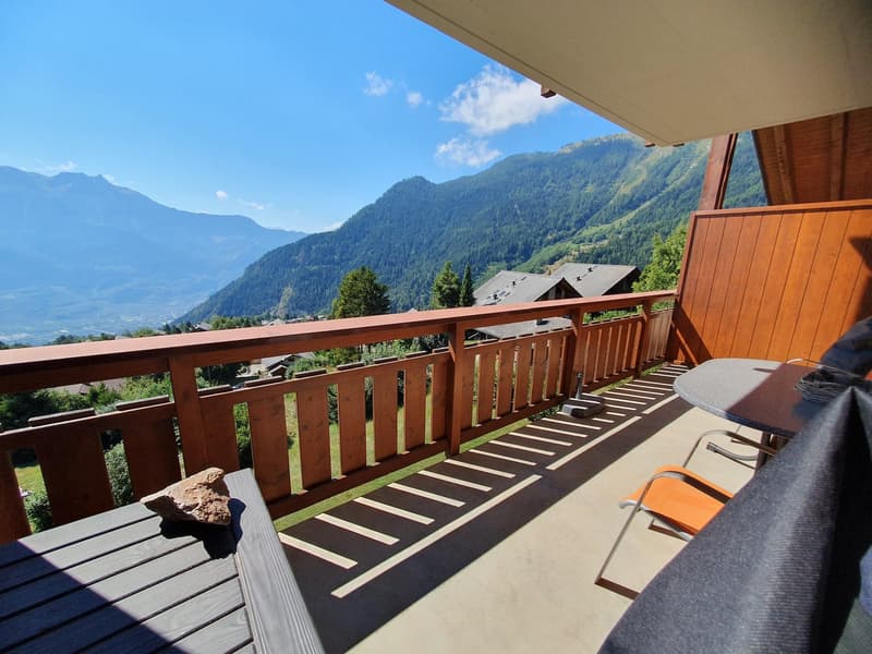 Wooden railing, table with chairs, table, grass, mountains, clear sky