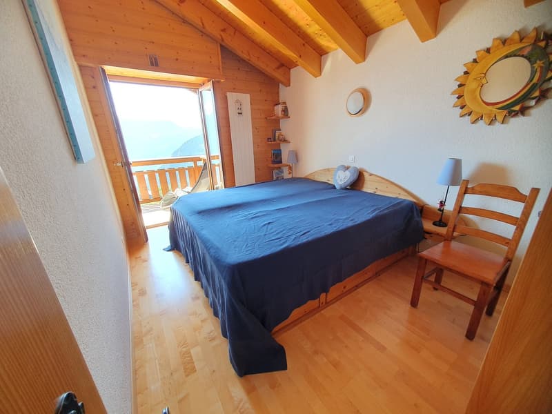 double bed with blue cover, wooden chair, table lamp, open door to balcony, wooden wall paneling, framed artwork