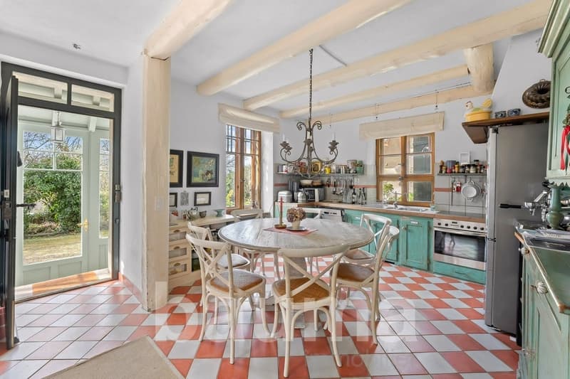 Chandelier, dining table, chairs, kitchen appliances, wooden beams, tiled floor