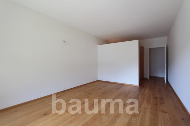 Empty room with white walls and hardwood flooring. The room appears to be a living room or bedroom with a doorway visible in the background.