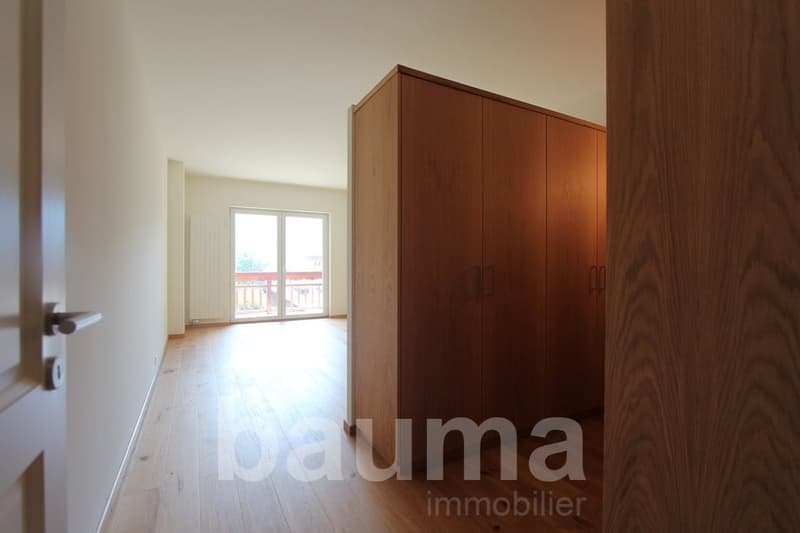 Spacious bedroom with wooden wardrobe, hardwood flooring, and large windows providing natural light and access to a balcony or terrace.