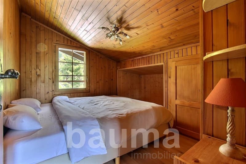 Cozy wooden bedroom with vaulted ceiling, large window, ceiling fan, and a fireplace