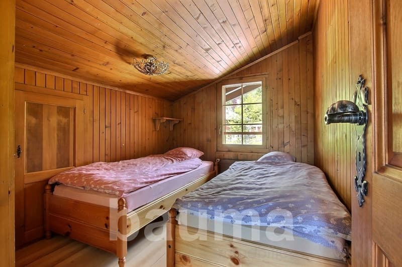 Cozy wooden bedroom with two twin beds, wooden paneled walls and ceiling, and a decorative fireplace on the wall.