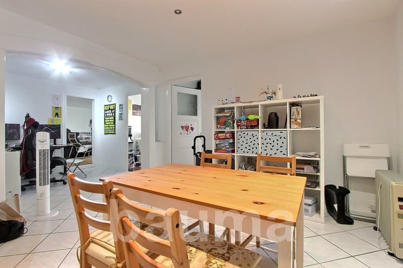 Dining room with wooden table, chairs, white tiled floor, white walls, white shelf, fan, radiator, and various items on the shelf
