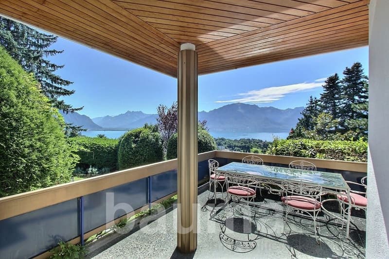 Balcony with wooden ceiling, glass table, chairs, view of mountains and lake