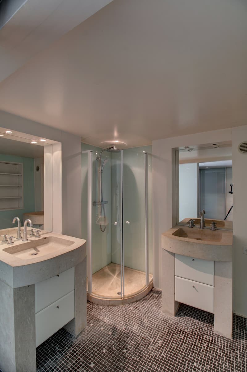 two sinks, a glass-enclosed shower, tile flooring, two large mirrors above sinks, two drawers under each sink, white fixtures and tiles