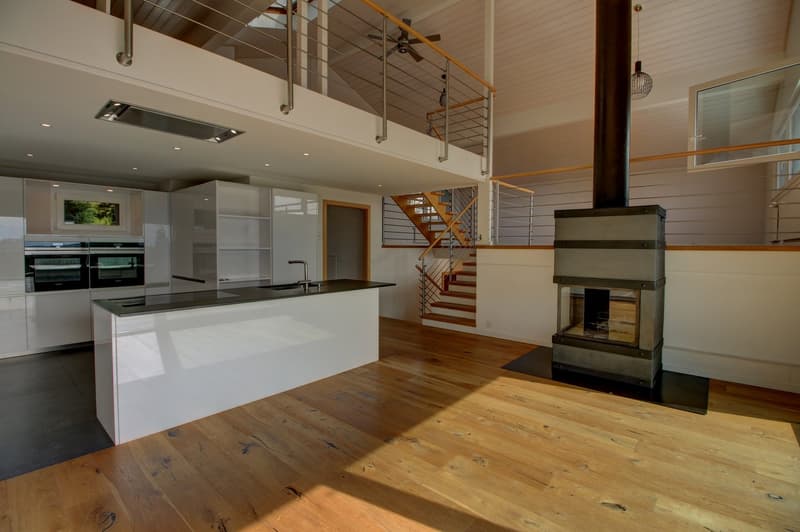 open kitchen, island with sink and stove, central fireplace, wooden flooring, balcony, railing, double ovens, cabinets, stairs