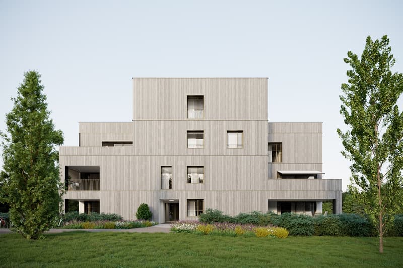 Multi-story building with a modern, minimalist design featuring a wooden facade, large windows, and balconies. The building is surrounded by a well-landscaped garden with trees and flowers.