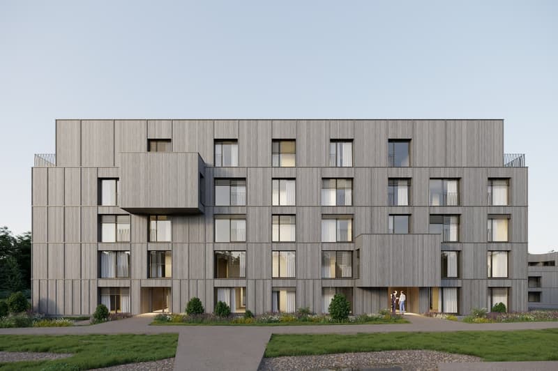 Multi-story apartment building with a modern, minimalist design. The building features a mix of wood and glass materials, with balconies or terraces visible on some of the units. The building is surrounded by a landscaped garden area with a paved walkway