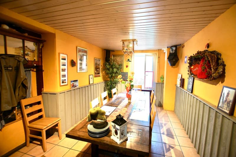 Dining room with a long wooden table, chairs, cactus, flowers, and picture frames on the wall