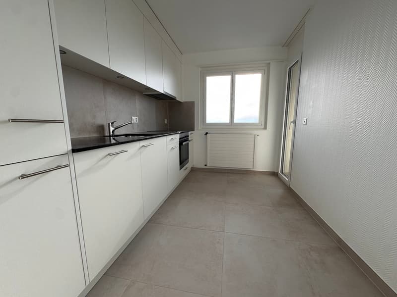 modern kitchen, white cabinets, tiled floor, window, black countertops, stainless steel faucet, oven, and white walls