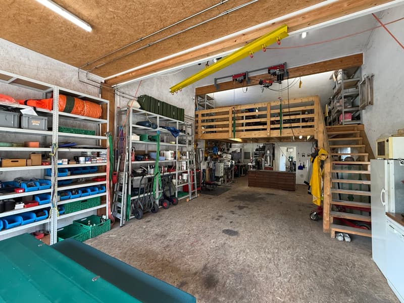 Spacious garage with shelves, storage boxes, ladders, carts, and a wooden platform.