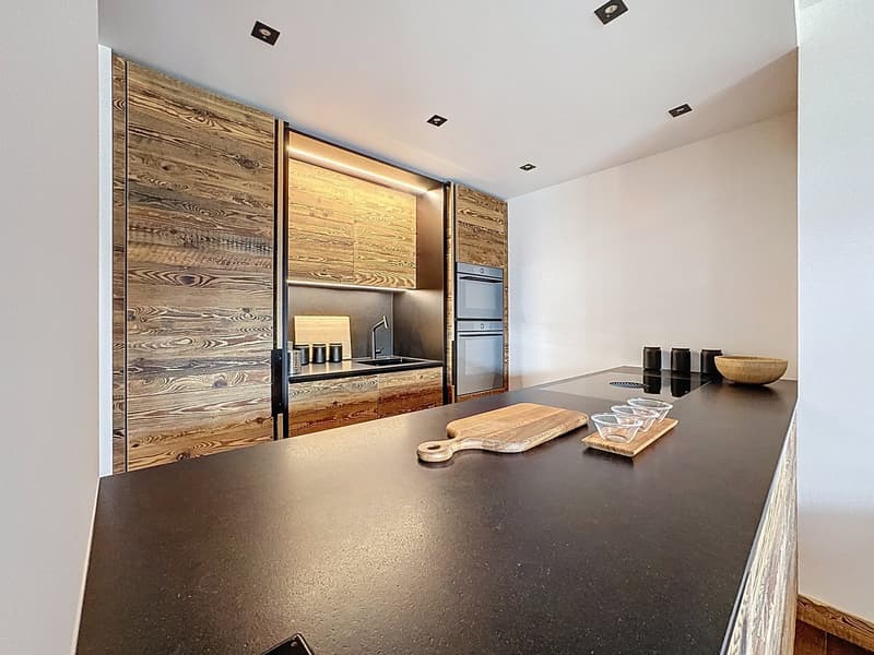 modern kitchen with black countertop, wooden wall cabinets, stainless steel sink, faucet, and appliances