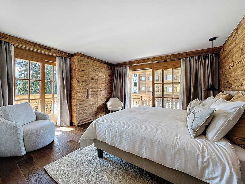 a large double bed, round armchair, white rug, gray armchair, wooden walls, large windows with view, large balcony