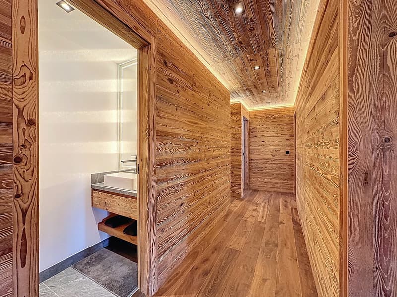 A hallway with wooden walls, wooden floor, a sink with faucet, and ceiling lights