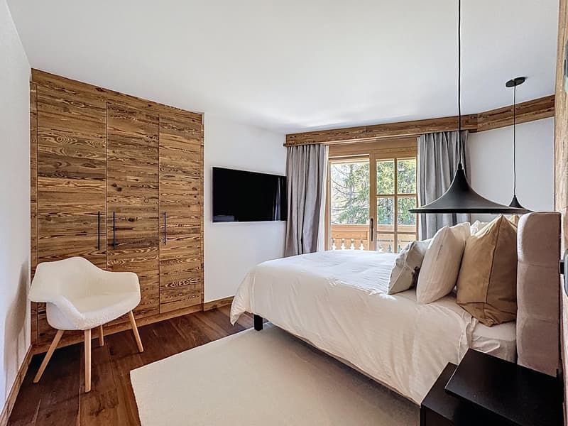 Wooden wall, bed, white pillow, white chair, television, white carpet, bedside table