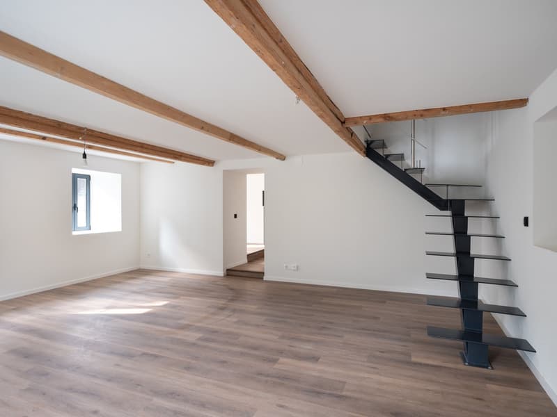 Empty room, hardwood floors, white walls, wooden beams, black metal staircase, small window